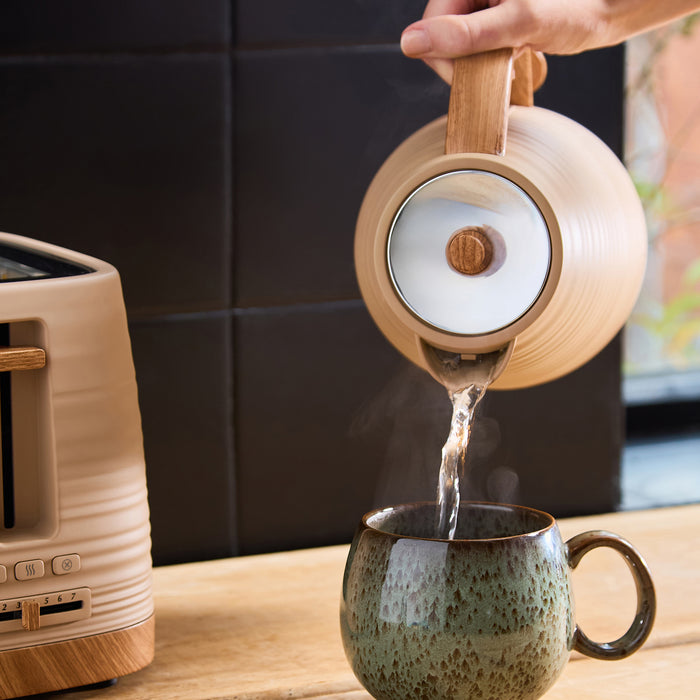 Person pouring water from a clay kettle into a ceramic mug on a kitchen counter.