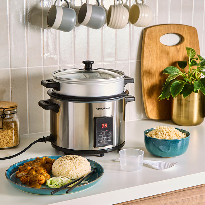 Stainless steel Morpy Richards rice cooker on a kitchen counter with food and utensils around