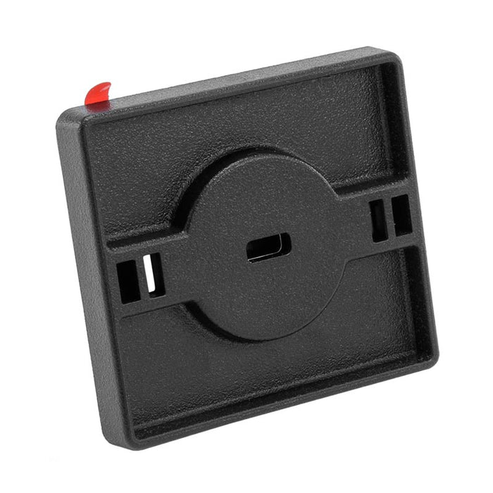 The Adhesive Security Plate with Slot for Use with Cables to Lock Down Laptops, Tablets, and Monitors is black, square, features a central circular indentation, a middle slot, two side openings, and a red tab at the top left.
