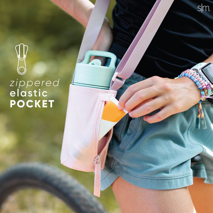 Pastel-colored kids' sling bag in light pink, mint green, and dusty blue with blurred green outdoor background