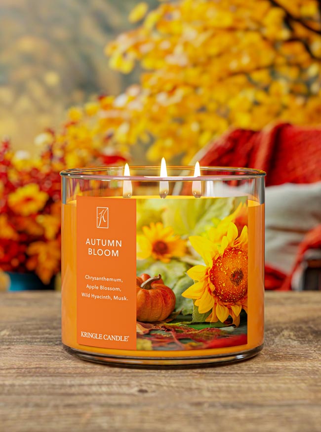 Kringle Candle Autumn Bloom candle on a wood table and fall background and with sunflower and pumpkin design on an orange label.