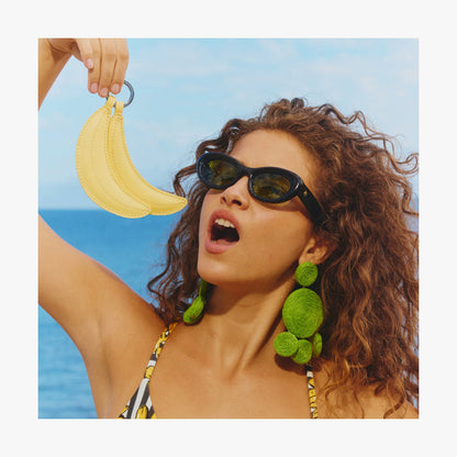 Banana | Woman standing by the ocean holding a Banana Charm like she is eating it