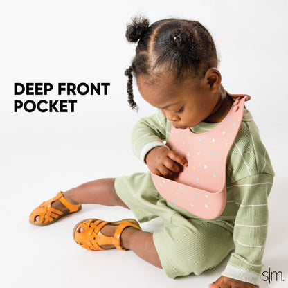 Toddler wearing sage green striped long-sleeve shirt and pale pink silicone bib with pocket, soft pastel colors