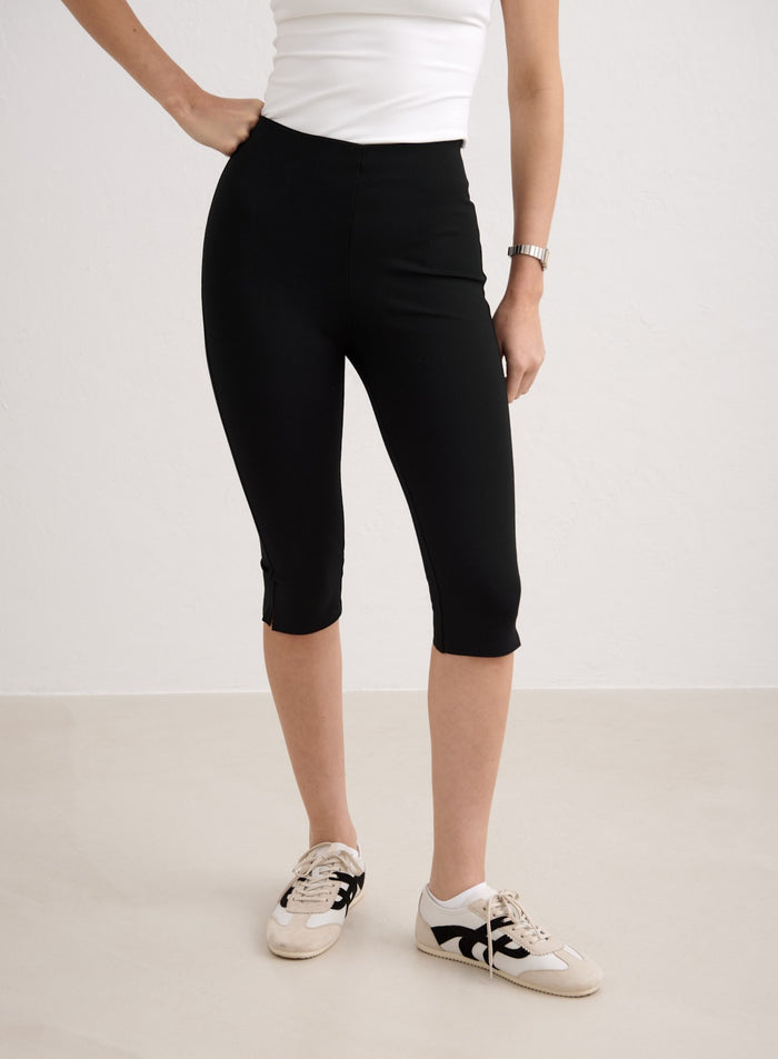 Sleek black Luxe Capri Pants by aim'n featuring a 3/4 length, styled with white sneakers. [34-174cm]