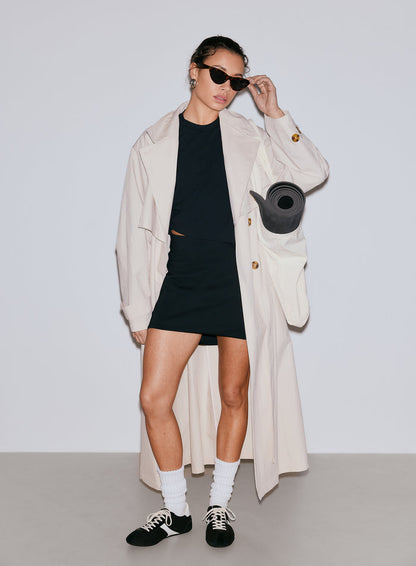 Woman in black Luxe Mini Skort, black top, and beige trench coat with a yoga mat [36-170CM]