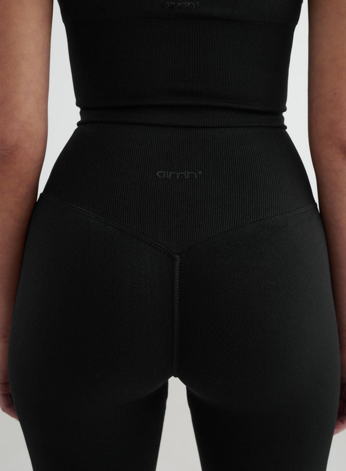 Black high-waisted seamless flare tights featuring a ribbed V-shaped waistband and tonal aim'n logo.