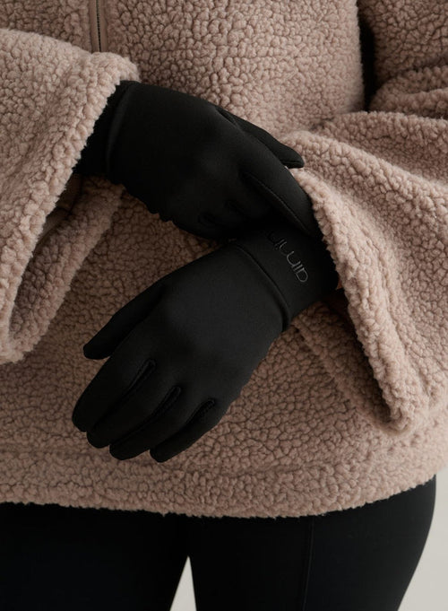 Black warming gloves featuring a tonal aim'n logo, paired with a cozy beige fleece jacket.