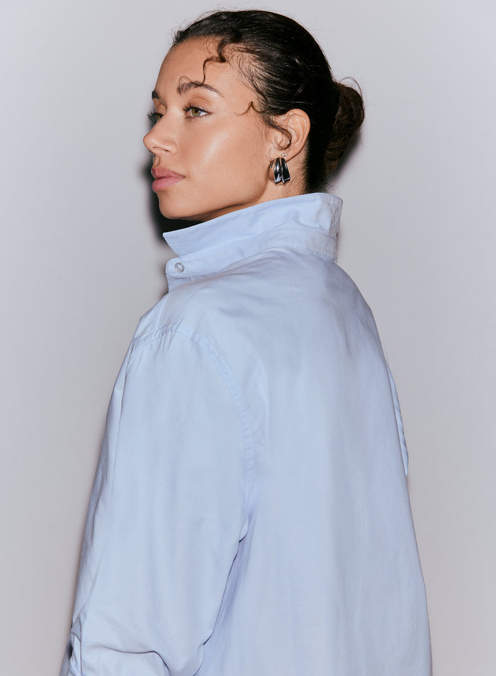 A woman wearing a light blue oxford shirt, shown from her right side, with her hair in a bun [M-170cm]