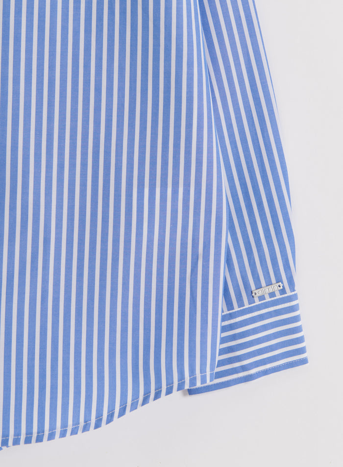 Close-up of the blue stripe poplin shirt's sleeve cuff and silver aim'n logo tag on crisp cotton fabric.
