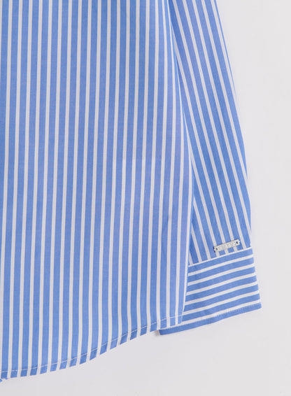 Close-up of the blue stripe poplin shirt's sleeve cuff and silver aim'n logo tag on crisp cotton fabric.