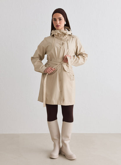 Woman wearing a cafe-au-lait Rain Jacket from aim'n with a waist tie and hood [M-174cm]