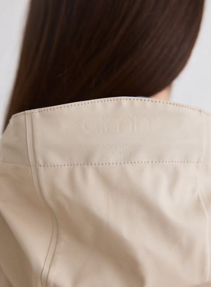 Close-up of the embossed aim'n logo on the back of the Cafe Au Lait Rain Jacket [M-174cm]