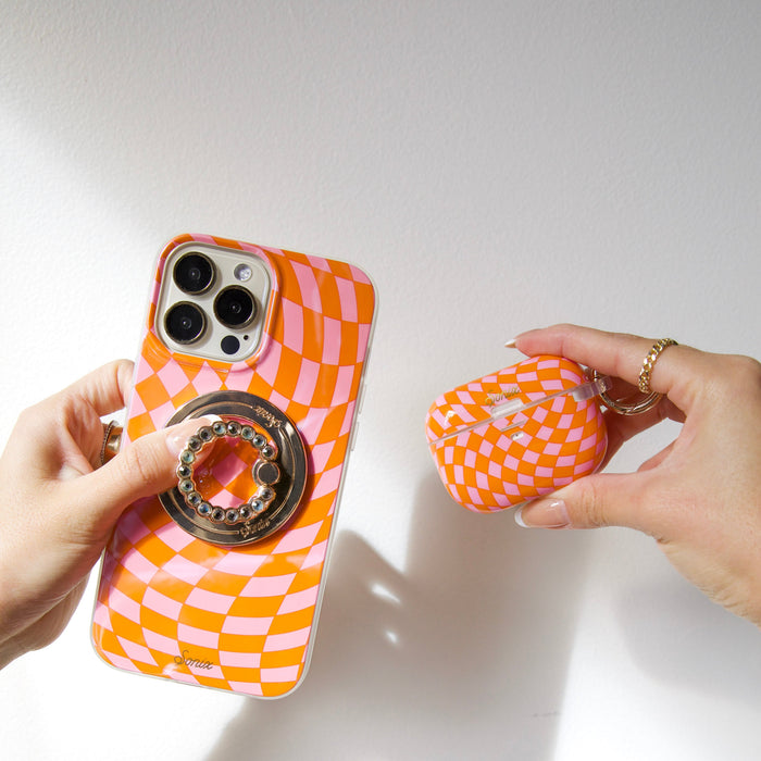 Close-up of pink and orange checkmate MagSafe iPhone case with ring grip and matching AirPods case on white background