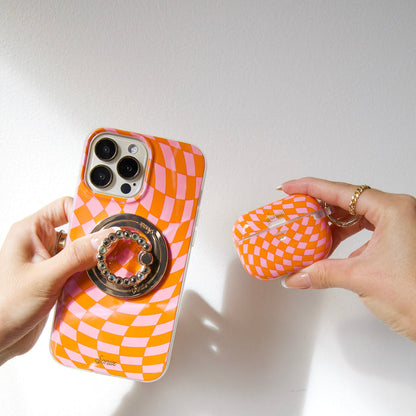 Close-up of pink and orange checkmate MagSafe iPhone case with ring grip and matching AirPods case on white background