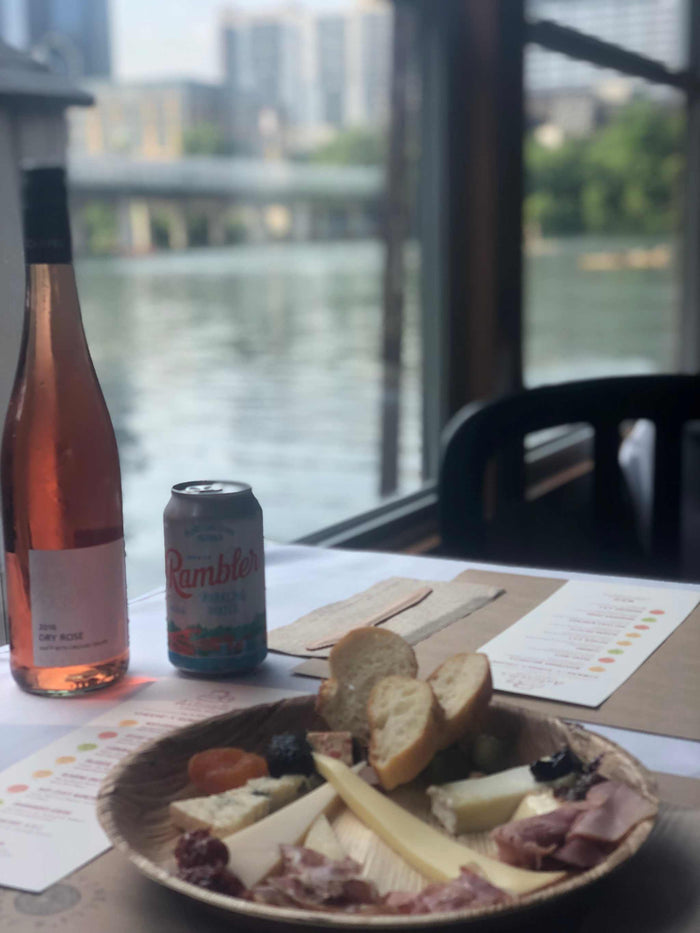 Image of cheese plate, bottle of wine, rambler on a boat