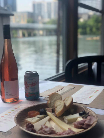 Image of cheese plate, bottle of wine, rambler on a boat