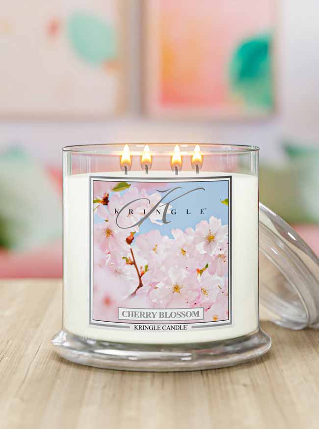 Kringle Candle cherry blossom 4-wick lit candle on a wooden surface with a blurred colorful background