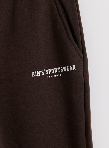 Close-up of chocolate brown Classic Sweatpants showing a side pocket and white aim'n logo on soft jersey.