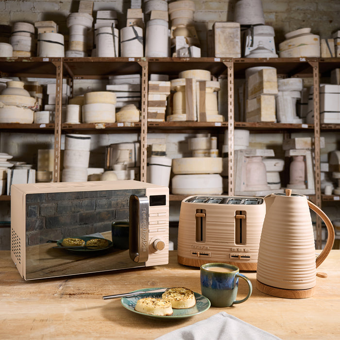 Kitchen appliances including a microwave, toaster, and kettle on a table with shelves of kitchenware in the background.