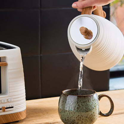 Person pouring water from a white kettle with wooden handle into a green mug on a kitchen counter.