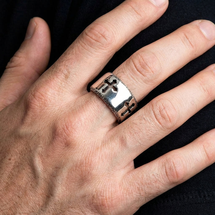 Wide sterling silver band ring with cut-out cross design worn on a man's finger against black shirt background, showcasing the polished metal finish and textured edges of this bold Christian biker ring