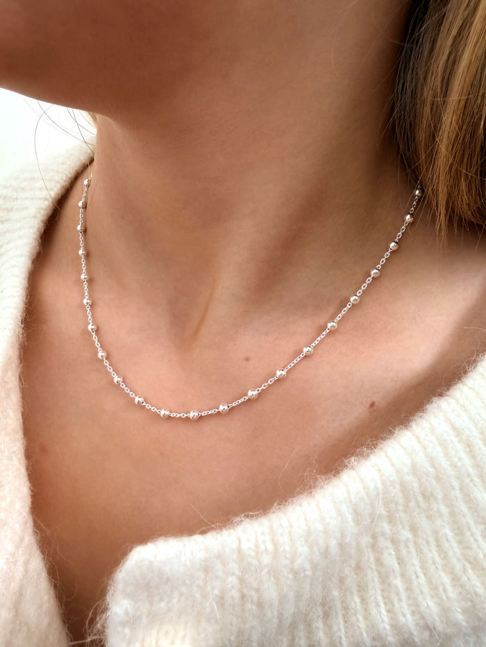 Tjej som bär ett kort, fint silverhalsband med tunn kedja och små silverkulor.