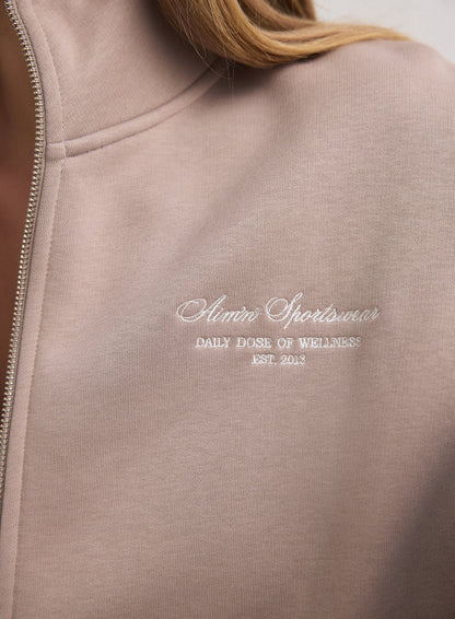 Close-up of the white aim'n script logo on a dark clay zip jacket made of soft cotton blend. [M-170cm]
