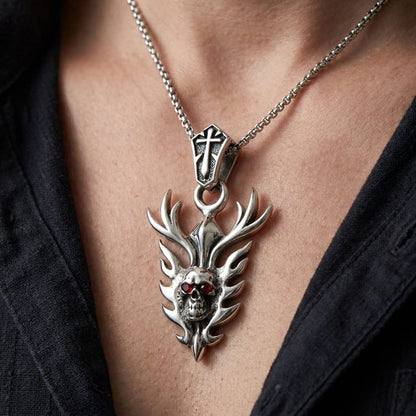 Close-up of a model wearing a silver flame skull biker pendant with red gemstone eyes and a cross bail on a chain necklace, styled with an open black shirt.