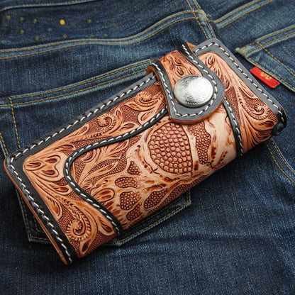 A men's hand-carved leather biker wallet with a demon skull design and silver concho, shown closed on blue jeans.