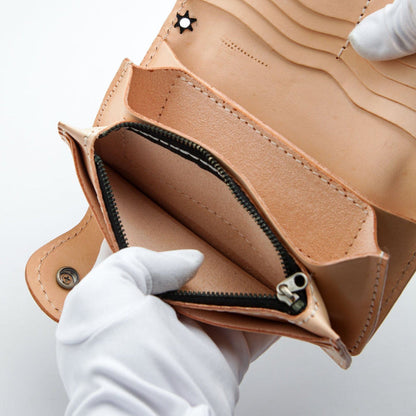 A gloved hand holding open the zippered coin pocket inside the natural leather wallet.