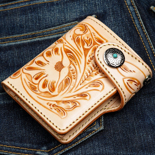 A handcrafted, hand-tooled western leather wallet with floral carving, shown on denim.