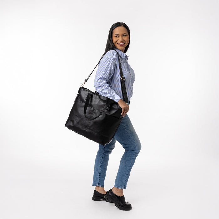 Black leather tote bag with soft blue and white striped button-up shirt and black footwear displayed on white background.