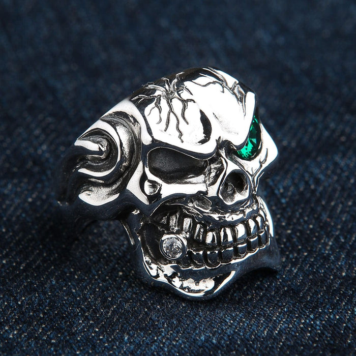 A solid silver gothic skull ring with a menacing grin and a single green gemstone eye.