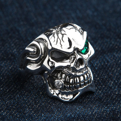 A solid silver gothic skull ring with a menacing grin and a single green gemstone eye.