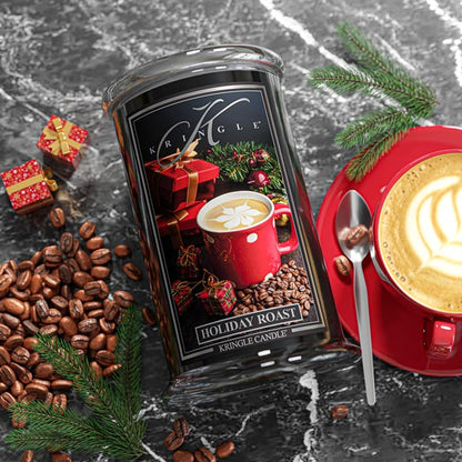 Kringle Candle Holiday Roast candle with coffee beans, a red mug, and Christmas decorations on a dark surface.