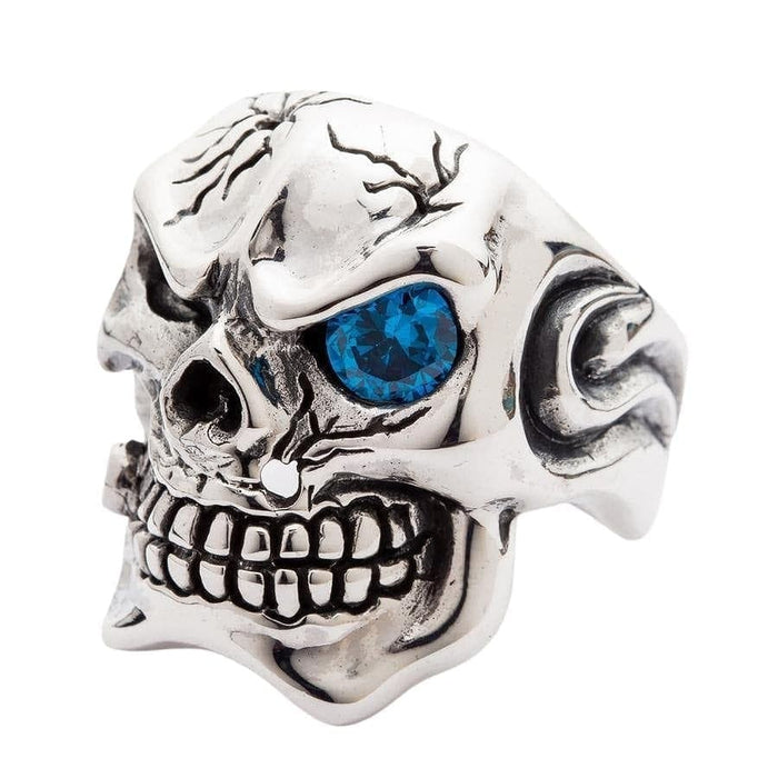 Three-quarter view of gangster skull ring highlighting cracked cranium and blue gemstone eye