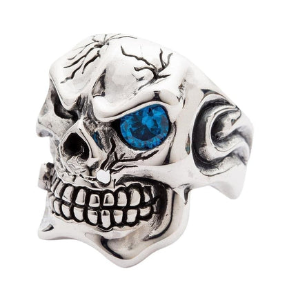 Three-quarter view of gangster skull ring highlighting cracked cranium and blue gemstone eye