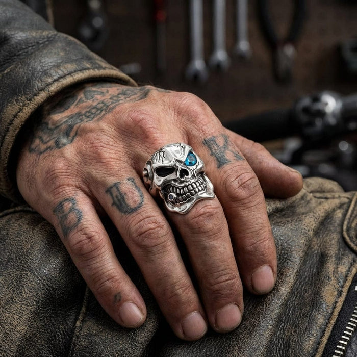 Biker skull ring on tattooed hand resting on vintage leather jacket in workshop setting