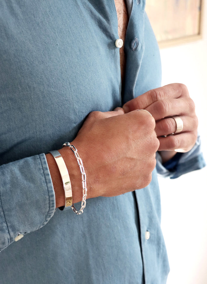 Man som bär ett stelt silverarmband, cuff tillsammans med ett kedjearmband i silver