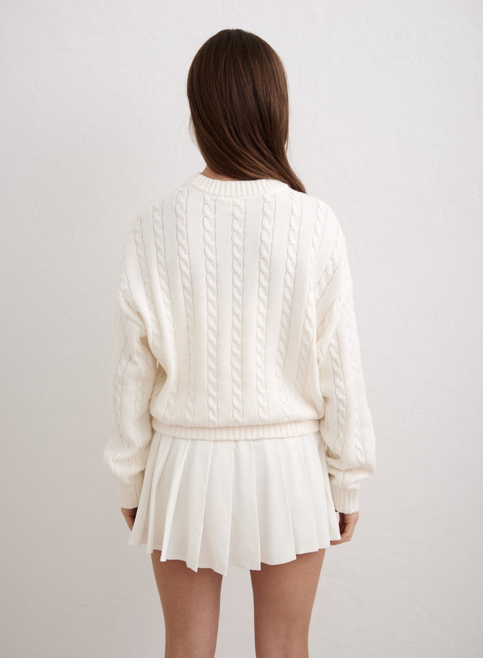 Off-white cable knit sweater by aim'n shown from the back, paired with a white pleated mini skirt. [M-174cm]