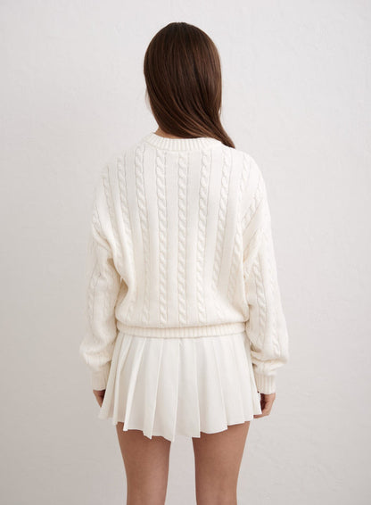 Off-white cable knit sweater by aim'n shown from the back, paired with a white pleated mini skirt. [M-174cm]