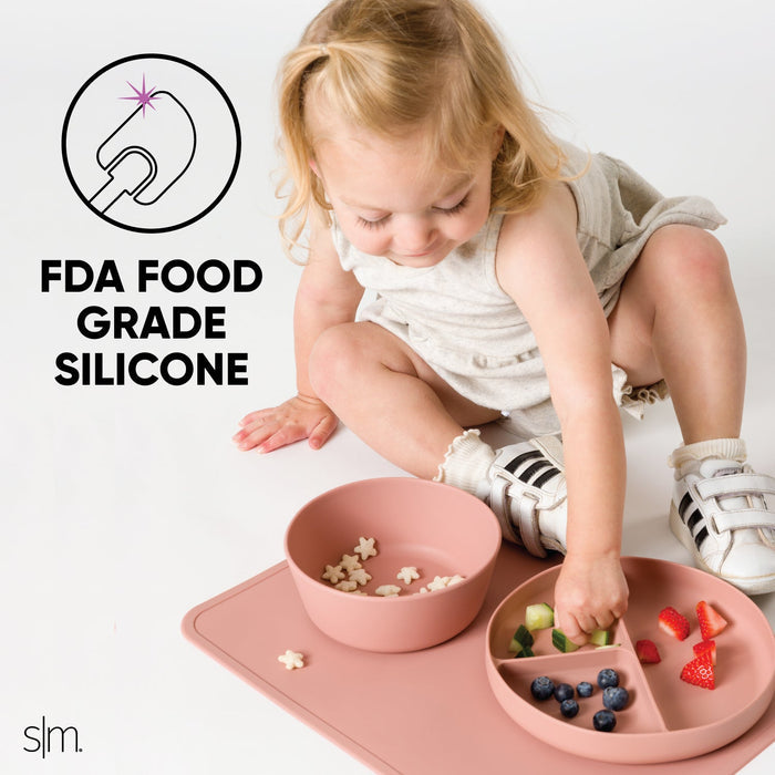 Toddler eating with FDA food-grade silicone dinnerware in dusty rose, wearing cream and beige clothing with white socks.