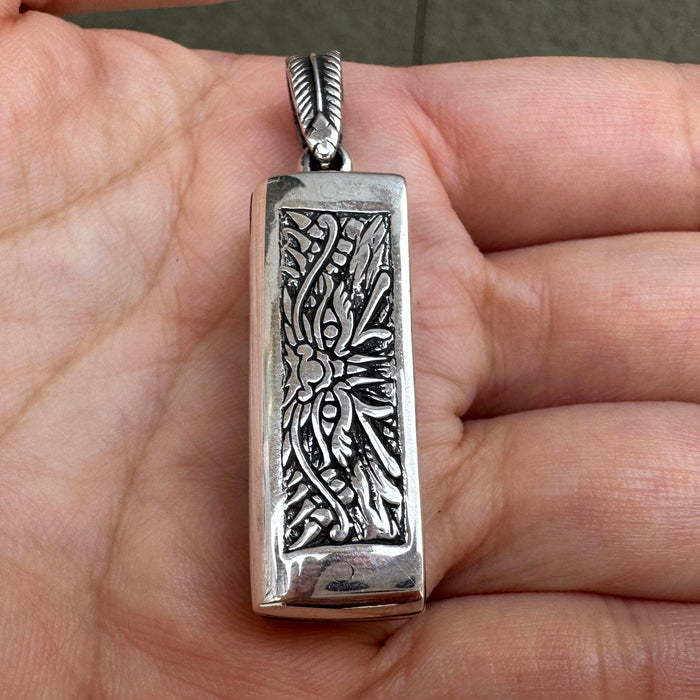 The front of the Japanese mini harmonica pendant held in hand, showing the intricate tribal demon face engraving.