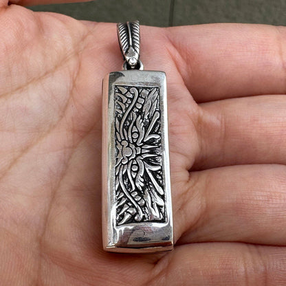 The front of the Japanese mini harmonica pendant held in hand, showing the intricate tribal demon face engraving.