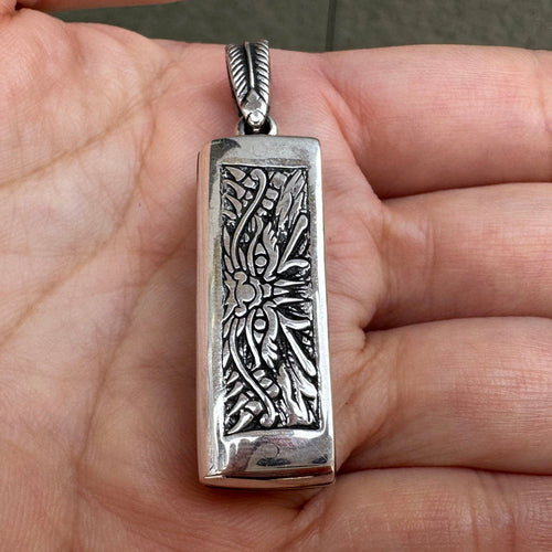 The front of the Japanese mini harmonica pendant held in hand, showing the intricate tribal demon face engraving.