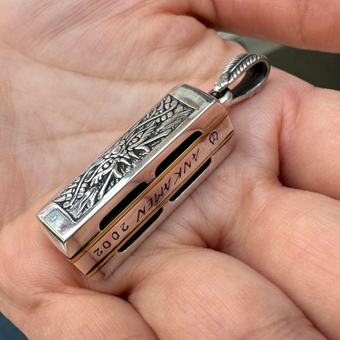 A side view of the playable harmonica pendant, showing the unique 'ANK AMEN 2002' artisan engraving.