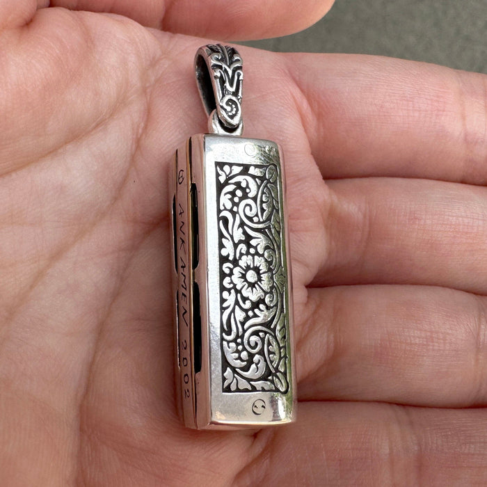 The reverse side of the sterling silver harmonica pendant, displaying the detailed floral and vine pattern.