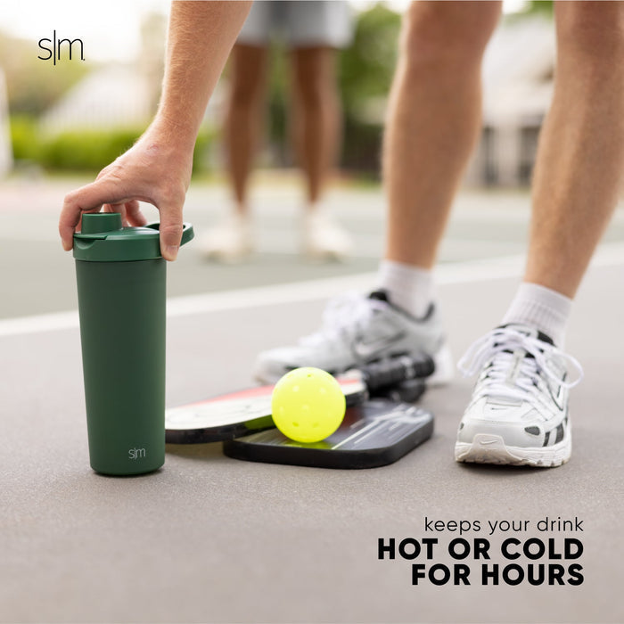 Forest green insulated tumbler next to white athletic shoes, white crew socks with black stripes, and light gray concrete pavement