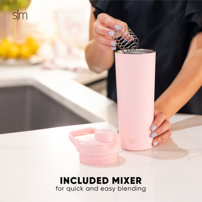 Pink ceramic mugs with white spoon on neutral kitchen countertop, person in black clothing visible, minimalist kitchen setting with soft pink and white color scheme.