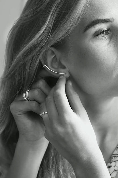 Tjej som tar på sig ett långt silverörhänge / ear climber som följer örats form.